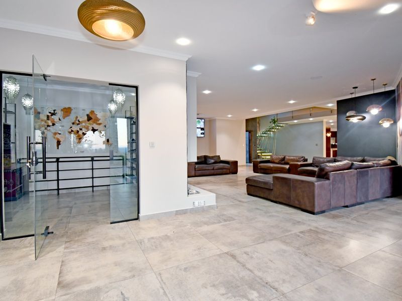 Spacious open-plan living area featuring large-format floor tiles, recessed lighting, and a modern glass-enclosed room with a feature wall.