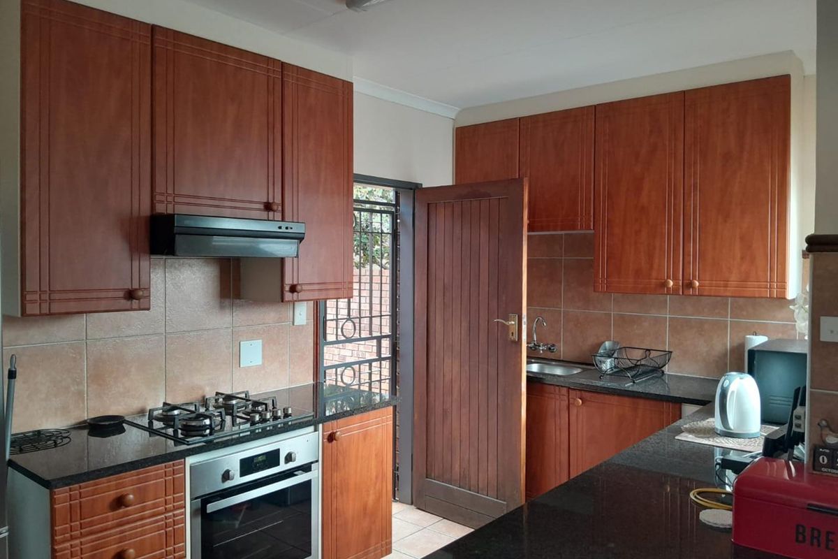 Functional kitchen featuring dark granite countertops, wood-finish cabinetry, built-in oven, gas hob, and an extractor fan with direct access to the exterior.