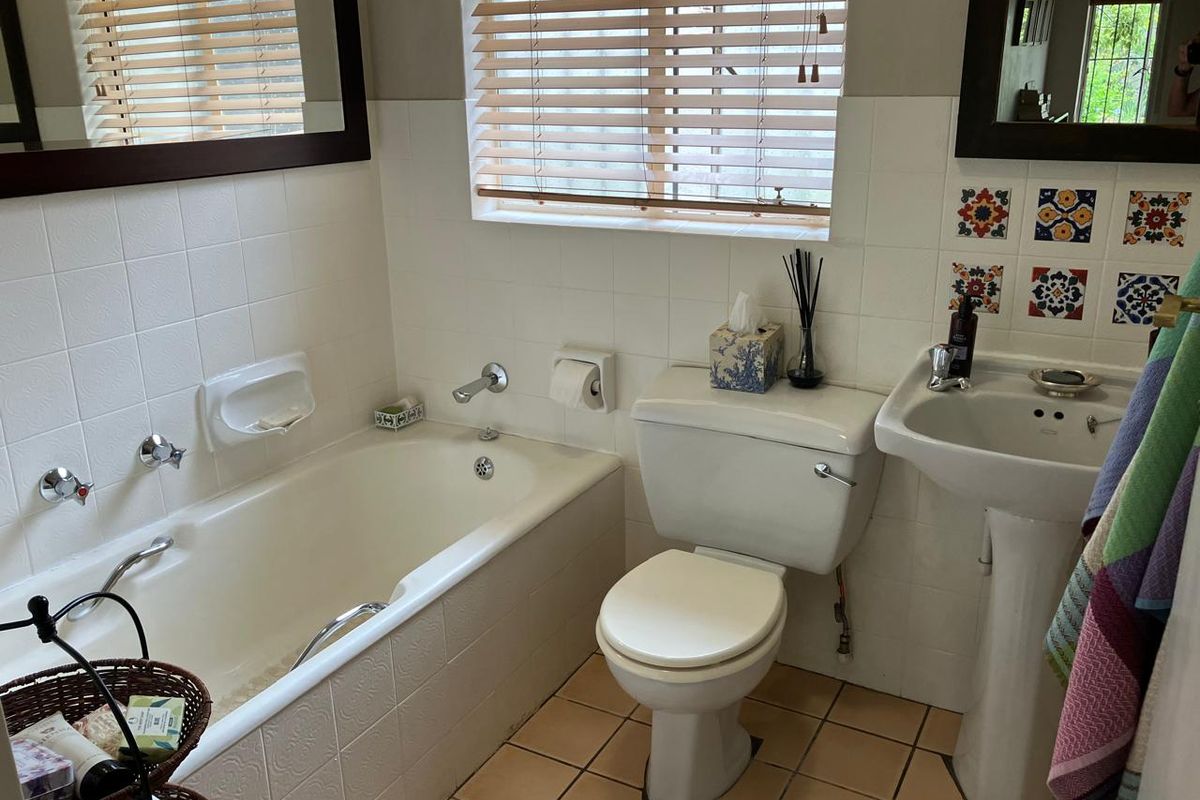 A functional bathroom featuring a bathtub, pedestal basin, toilet, and tiled finishes with decorative accent tiles.