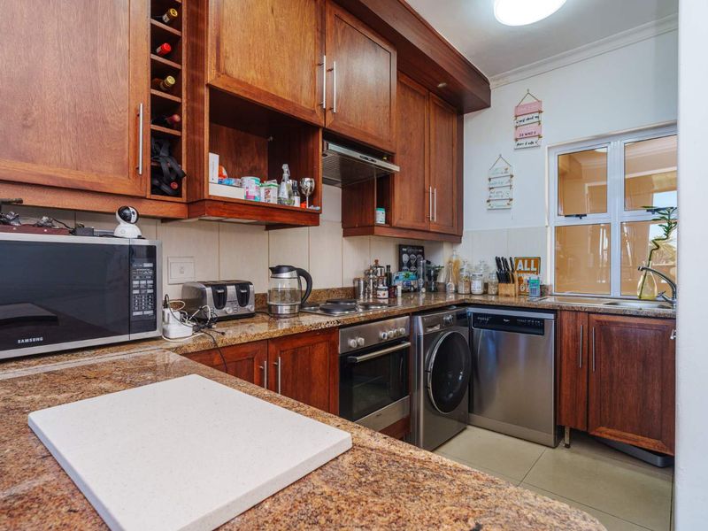 A functional kitchen featuring warm wooden cabinetry, granite countertops, and integrated appliances including an oven, hob, extractor fan, dishwasher, and washing machine.