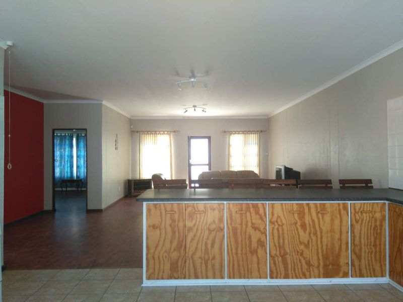 Spacious open-plan living area featuring a kitchen island, laminate and tiled flooring, and neutral wall finishes with direct access to adjacent rooms.
