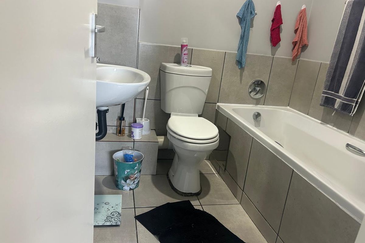 A functional bathroom featuring a standard bathtub, pedestal basin, and toilet with neutral wall and floor tiling.