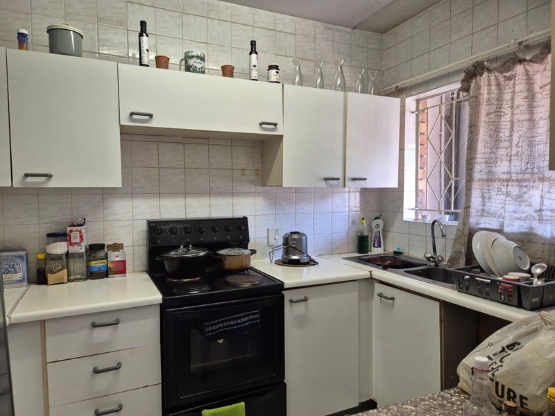 A functional kitchen featuring white cabinetry, laminate countertops, a stainless steel sink, and a freestanding stove, with tiled walls and a window security gate.
