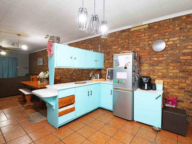 Open plan kitchen and dining area featuring exposed brick walls, tiled flooring, and light blue cabinetry with a functional layout.