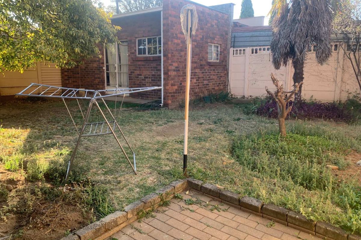 Rear garden area featuring a brick exterior facade, paved patio section, and precast boundary walling in need of maintenance.