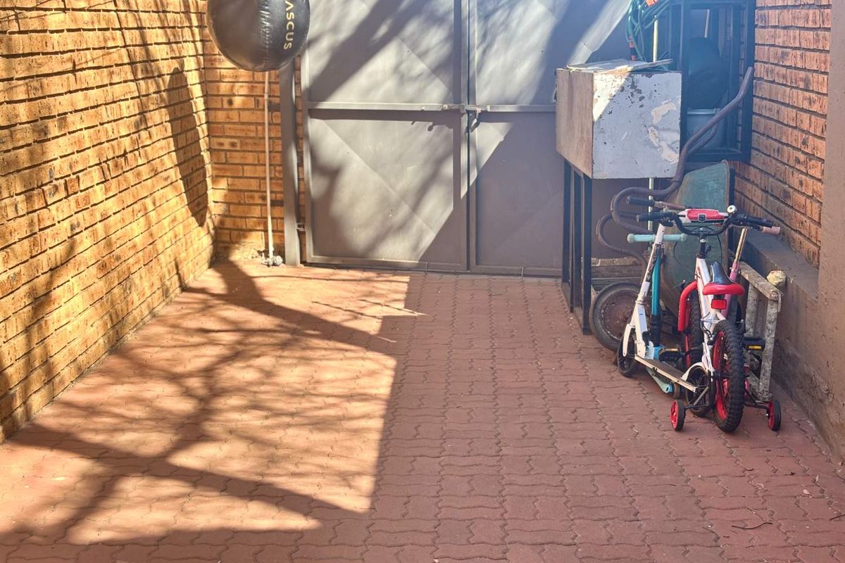 A paved rear courtyard area enclosed by brick boundary walls and a metal gate, offering a functional outdoor space.