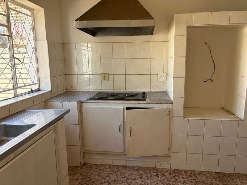 A dated kitchen featuring built-in cabinetry, an electric hob with extractor fan, and a stainless steel sink, requiring renovation and cosmetic updates.