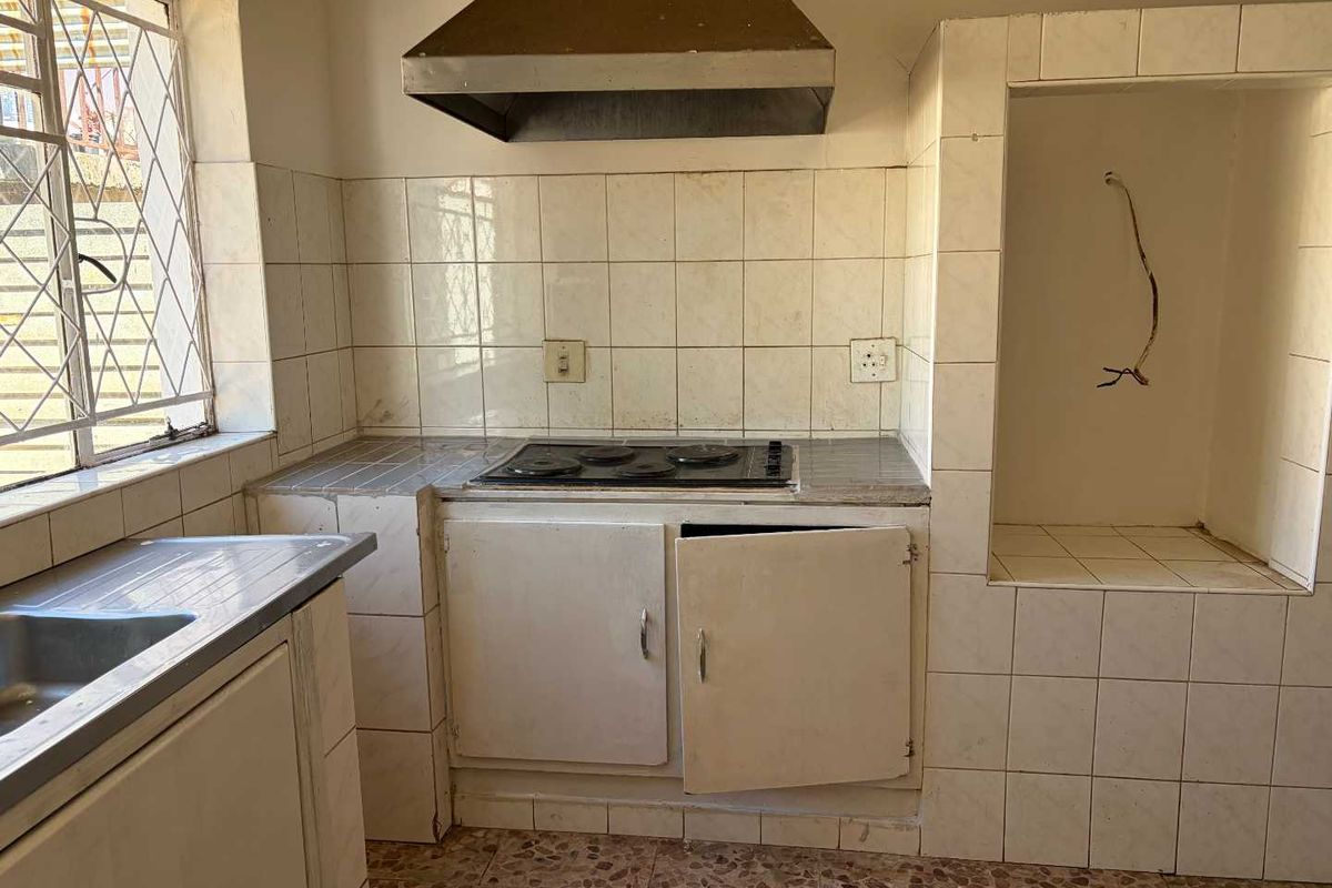 A dated kitchen featuring built-in cabinetry, an electric hob with extractor fan, and a stainless steel sink, requiring renovation and cosmetic updates.