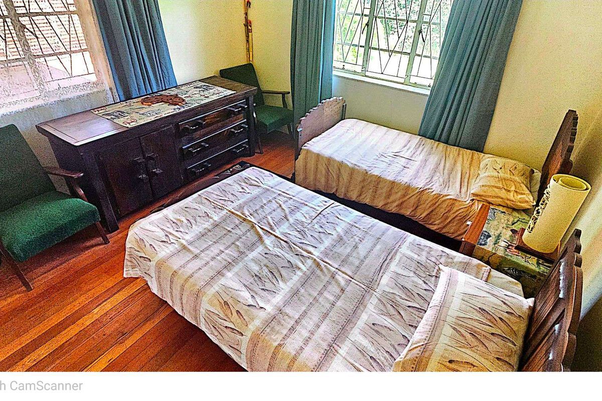 A bedroom featuring timber flooring and large windows with security bars, providing natural light and a functional layout.