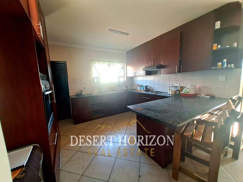 A functional kitchen featuring dark wood cabinetry, granite countertops, a built-in oven, and tiled flooring with a breakfast nook area.