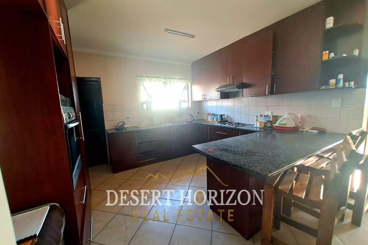 A functional kitchen featuring dark wood cabinetry, granite countertops, a built-in oven, and tiled flooring with a breakfast nook area.