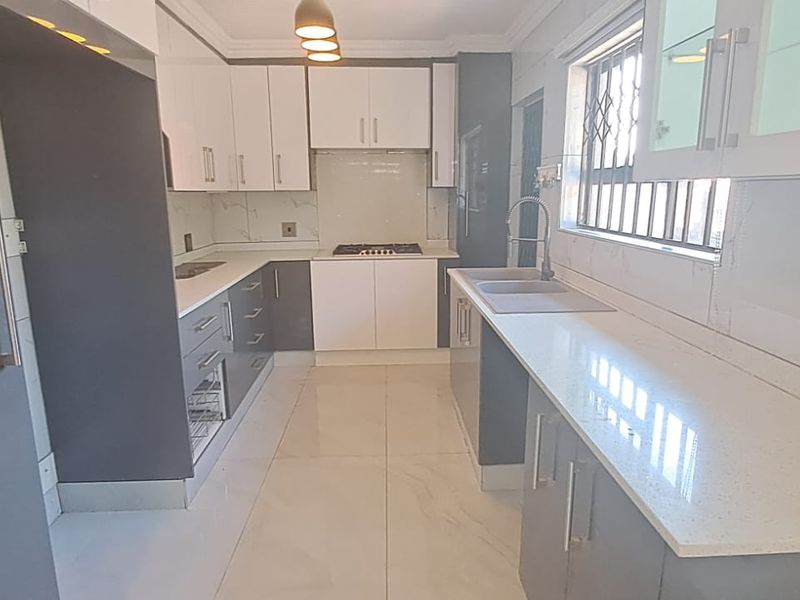 Modern galley-style kitchen featuring high-gloss cabinetry, stone countertops, marble-look wall tiles, and a gas hob, presenting a clean and contemporary finish.