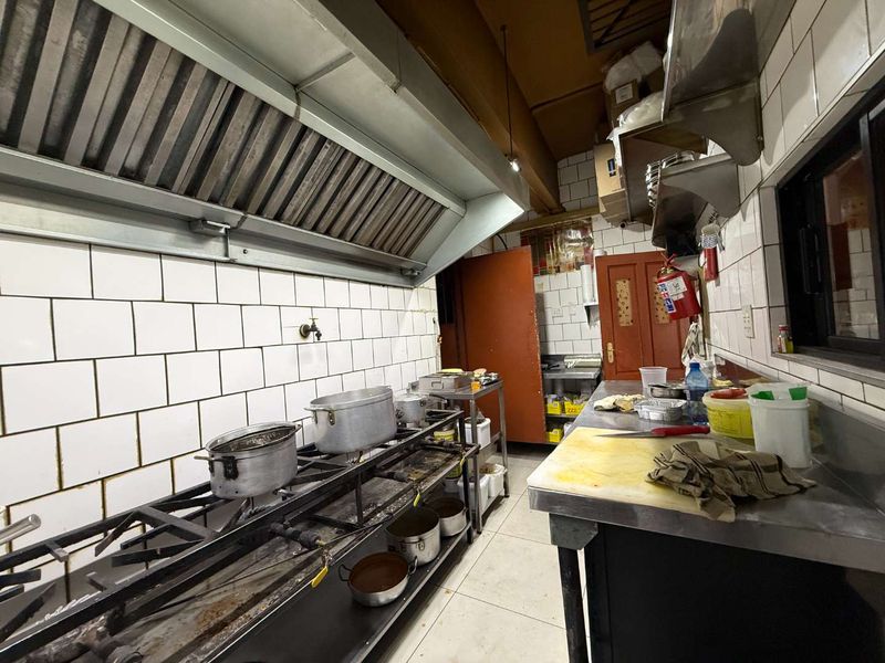 Commercial kitchen space featuring a large extractor hood, gas cooktop, stainless steel prep surfaces, and tiled wall finishes.