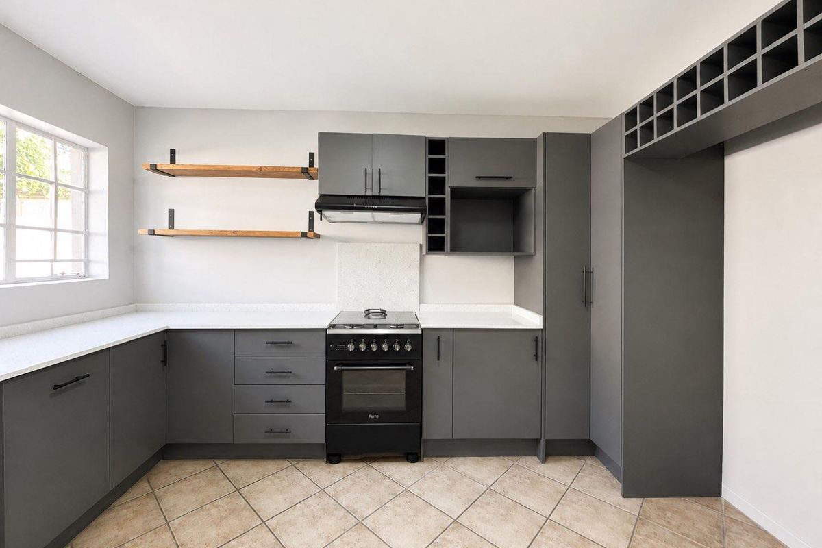 Modern kitchen featuring dark grey cabinetry, stone countertops, a freestanding stove with extractor fan, and open shelving, finished with tiled flooring.