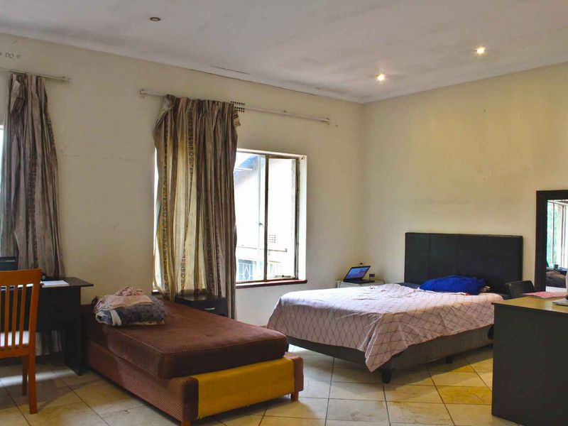 Spacious bedroom featuring tiled flooring and recessed downlighting, offering a functional layout with natural light from multiple windows.