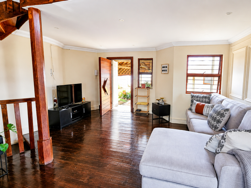 A living room featuring dark wooden flooring, wainscoting, and a prominent wooden staircase, with direct access to an outdoor area.