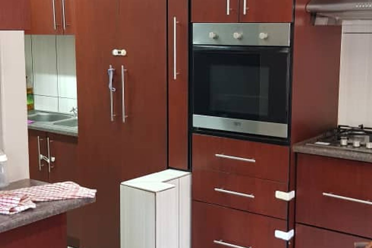 A functional kitchen featuring dark wood-toned cabinetry, built-in oven, gas hob, extractor fan, and tiled flooring.