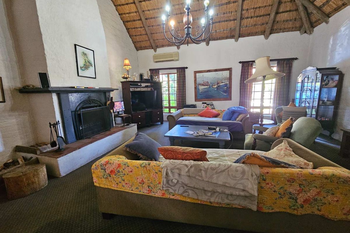 Spacious living room featuring a high thatched ceiling with exposed timber rafters, a large masonry fireplace, and a wrought iron chandelier.