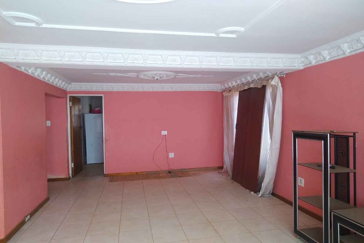 Spacious living area featuring decorative ceiling cornices, ceiling roses, and tiled flooring, offering a blank canvas for renovation and interior design updates.