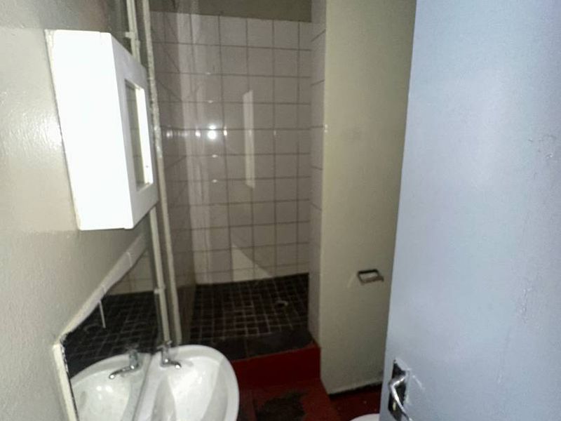 A small, dated bathroom featuring a pedestal basin, toilet, and a tiled shower cubicle, currently in need of renovation and repair.
