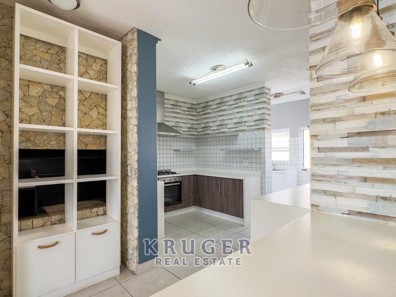 A modern kitchen featuring stone-clad feature walls, built-in shelving, dark wood cabinetry, and integrated appliances, offering a clean and functional cooking space.