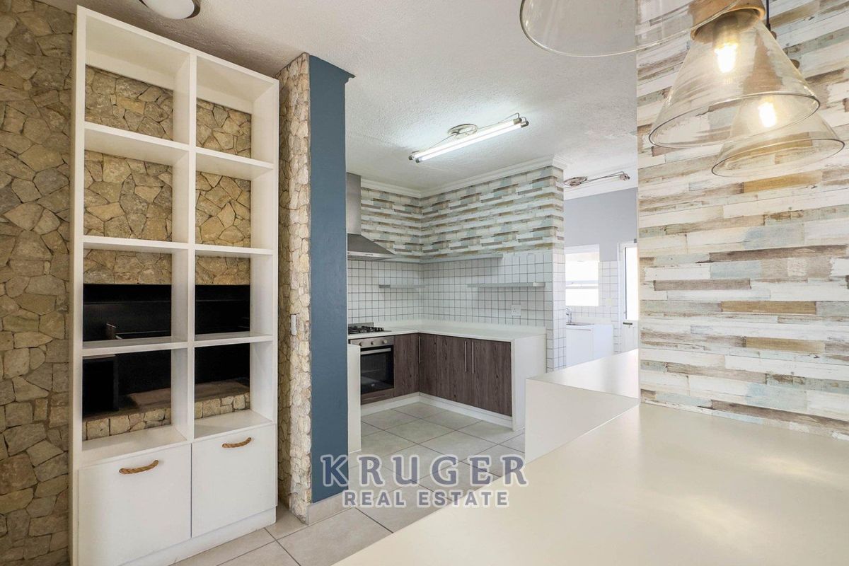 A modern kitchen featuring stone-clad feature walls, built-in shelving, dark wood cabinetry, and integrated appliances, offering a clean and functional cooking space.