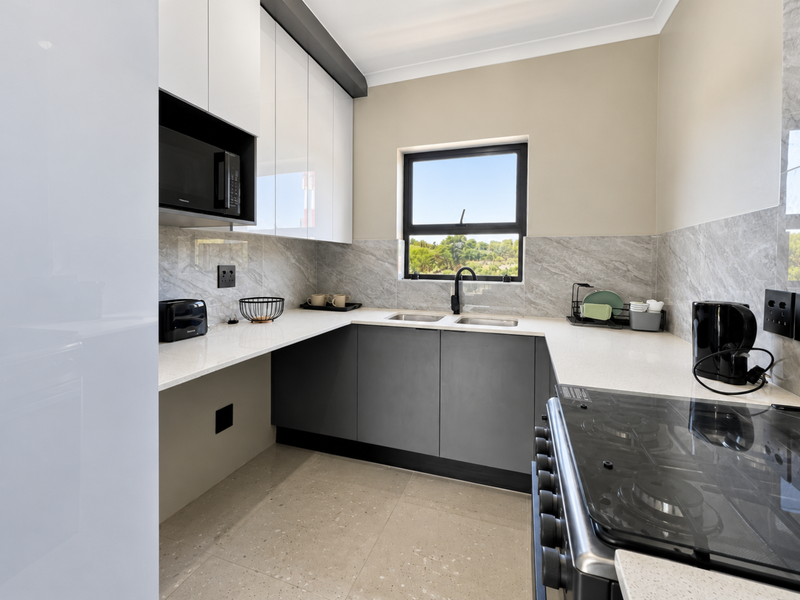 Modern kitchen featuring sleek two-tone cabinetry, stone countertops, marble-look splashback, and high-quality built-in appliances with a functional U-shaped layout.