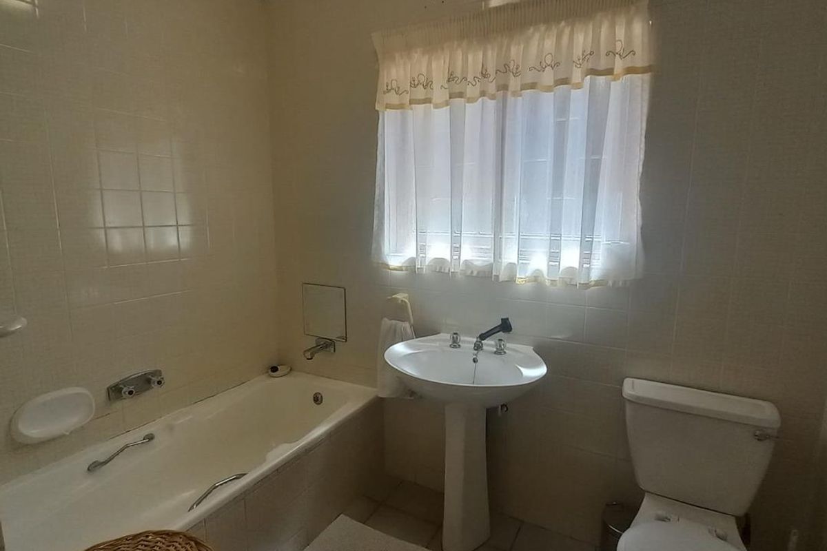 A functional bathroom featuring a built-in bathtub, pedestal basin, and toilet, finished with neutral wall tiles and tiled flooring.