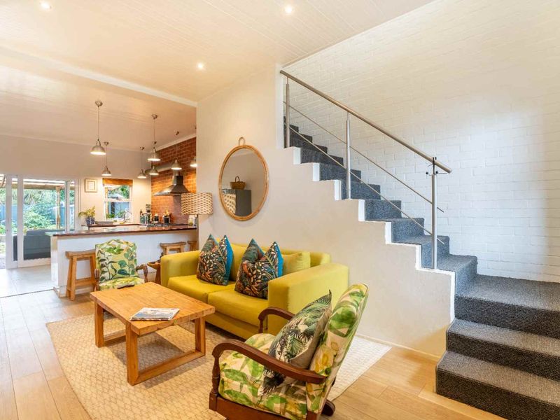 Bright open-plan living area featuring a modern staircase with stainless steel railing, exposed brick accents, and a seamless flow into the kitchen space.