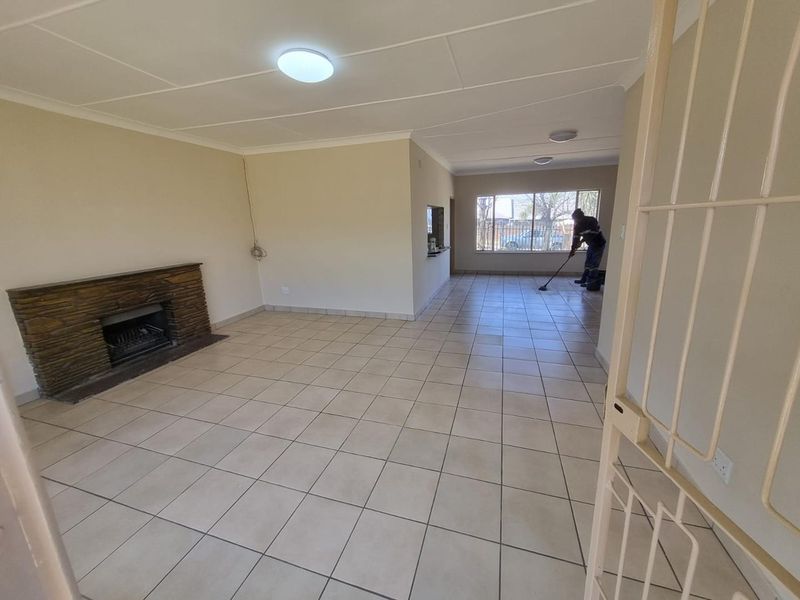 Spacious open-plan living area featuring ceramic floor tiles, a stone fireplace, and neutral wall finishes, offering a bright and versatile layout.