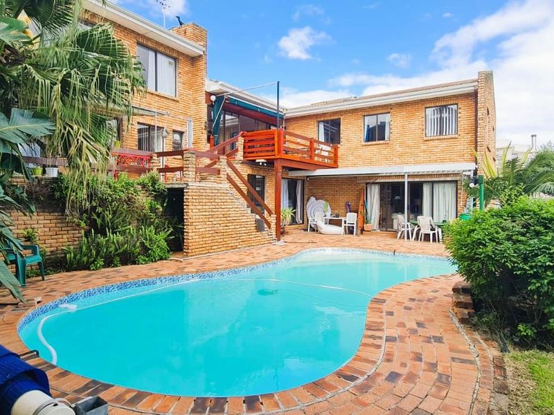 Rear exterior view of the apartment building featuring a swimming pool, brick paved surround, and a raised wooden deck balcony.