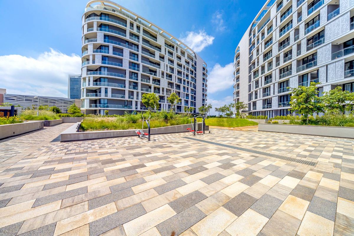A well-maintained paved courtyard and landscaped garden area situated between modern apartment buildings, featuring outdoor fitness equipment and clean architectural lines.
