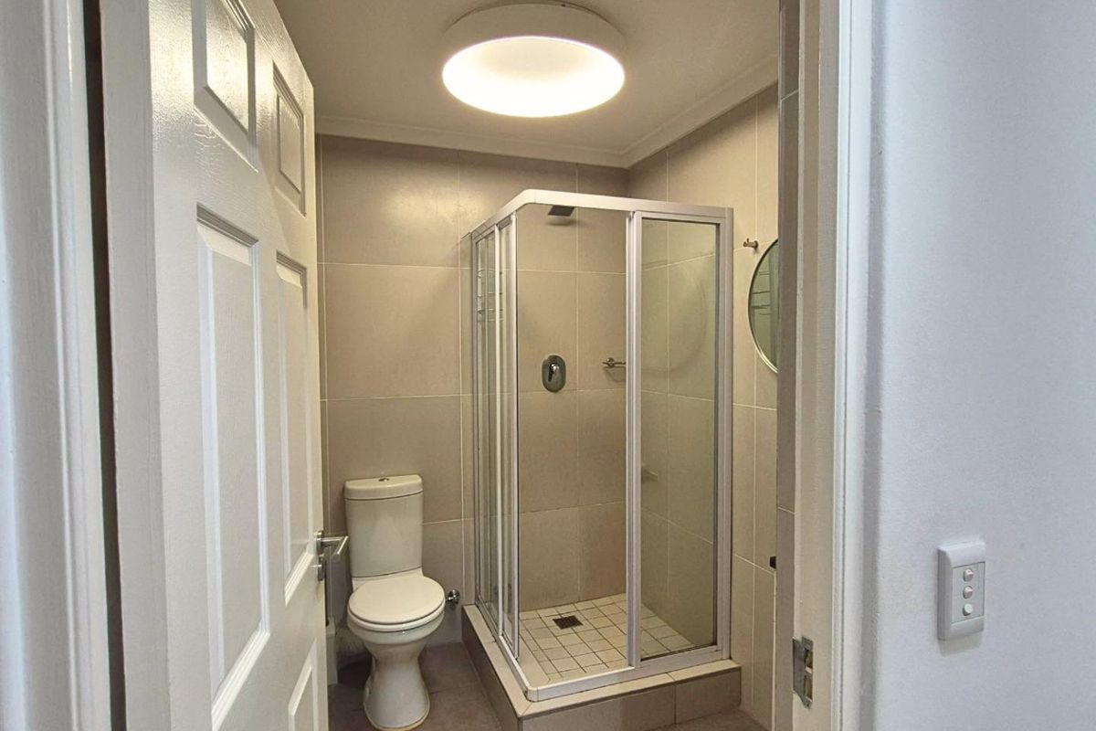A compact, functional bathroom featuring a corner shower enclosure, a standard toilet, and neutral wall and floor tiling.