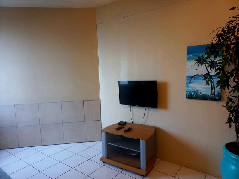 A living area featuring ceramic floor tiles, a wall-mounted television, and a partially tiled wall section, requiring cosmetic updates to improve the overall aesthetic.