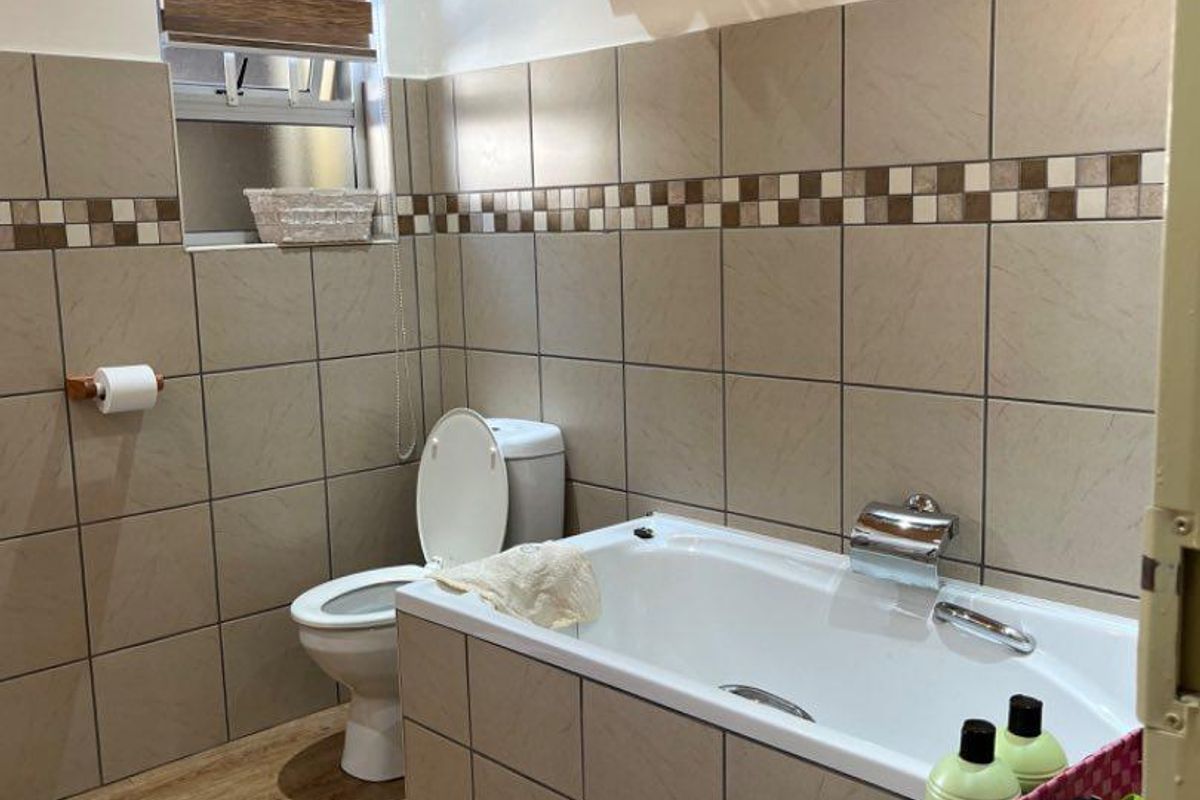 A functional bathroom featuring tiled walls with a decorative border, a built-in bathtub, a toilet, and wood-look flooring.