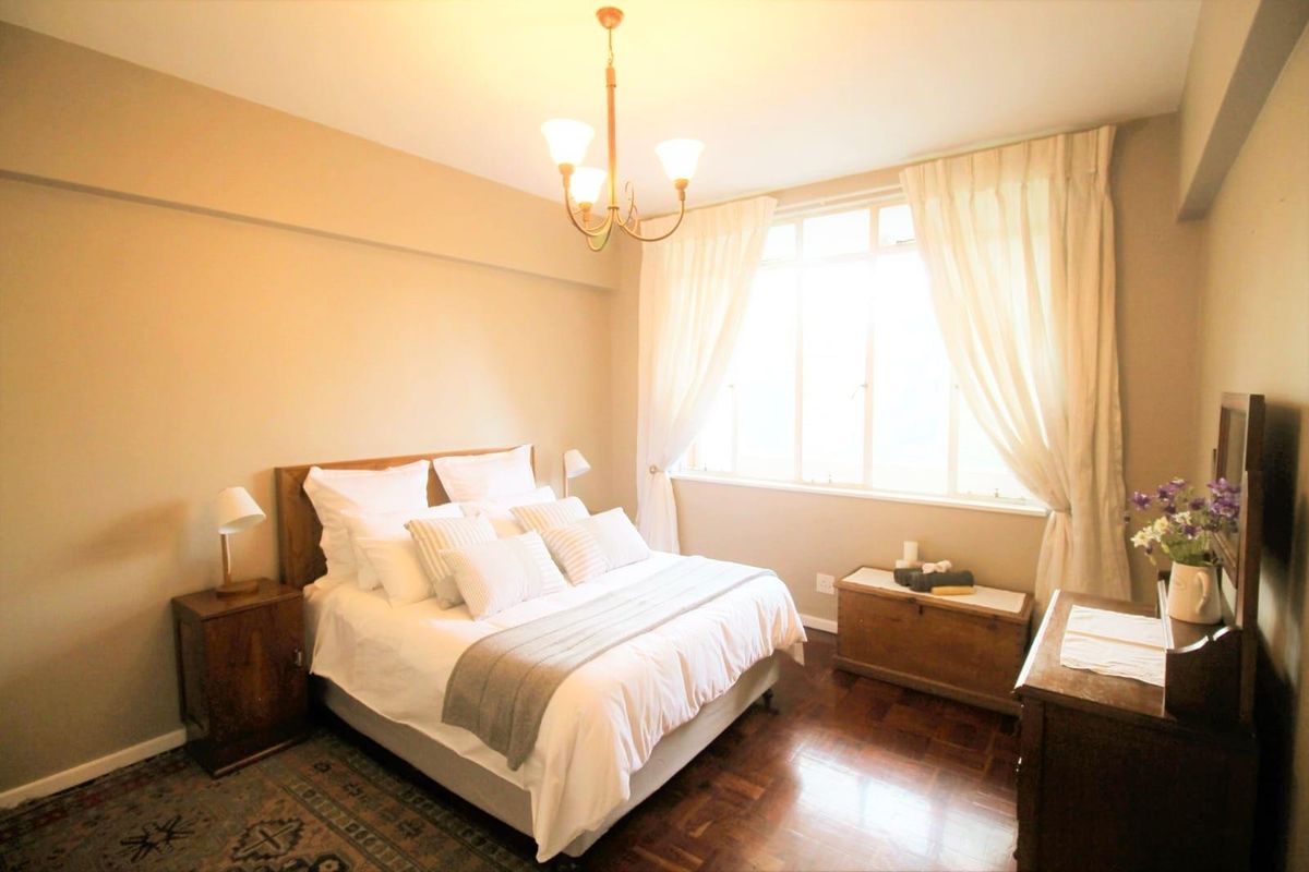 A well-maintained bedroom featuring polished parquet flooring, neutral wall tones, and a large window allowing for ample natural light.