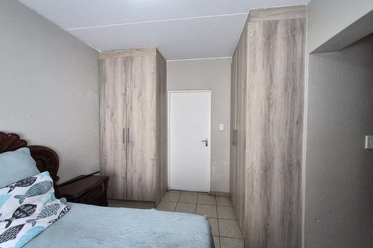 A bedroom featuring light wood-grain built-in cupboards and neutral tiled flooring.