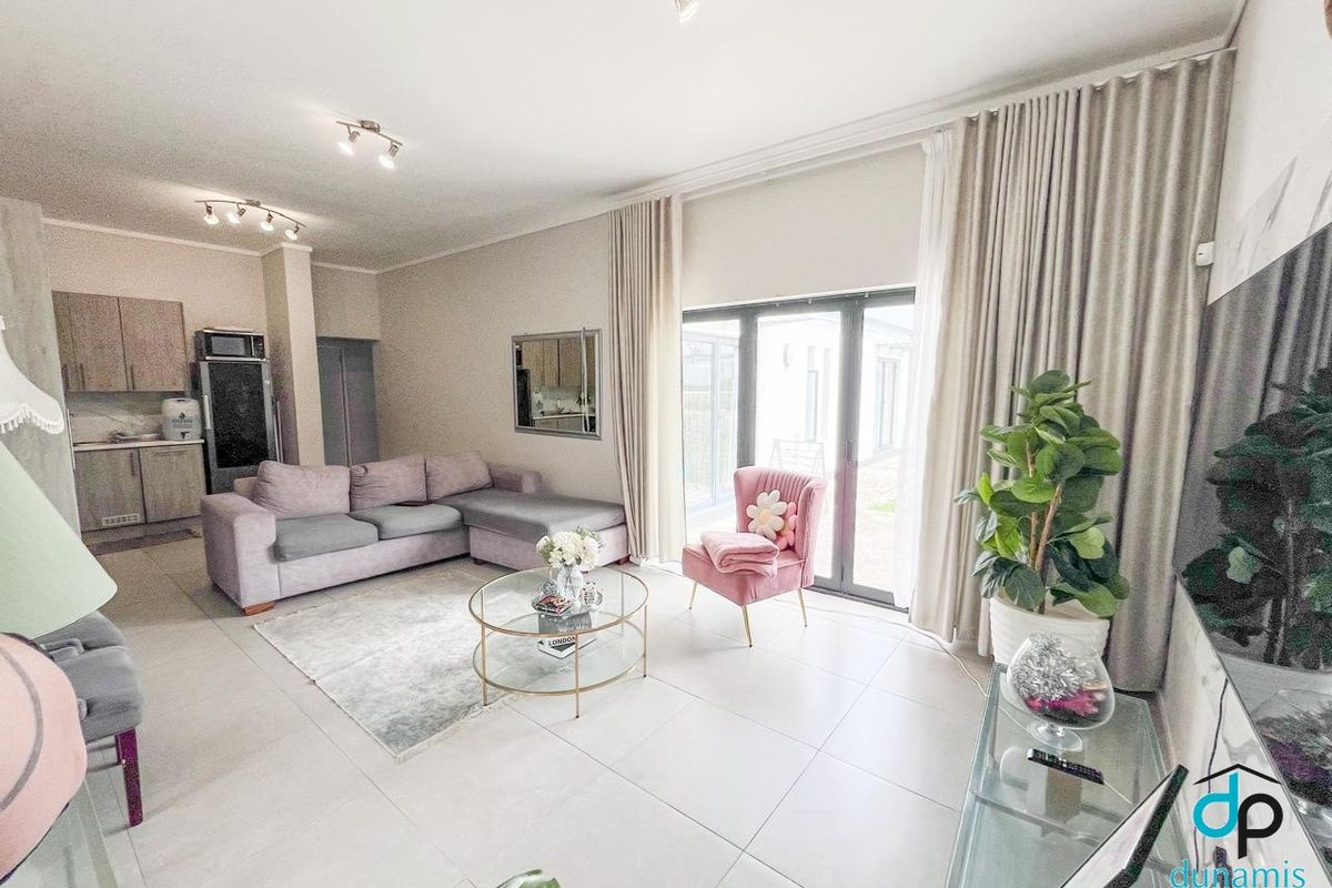 A bright open-plan living area featuring large format floor tiles, modern kitchen cabinetry, and expansive sliding glass doors leading to the exterior.