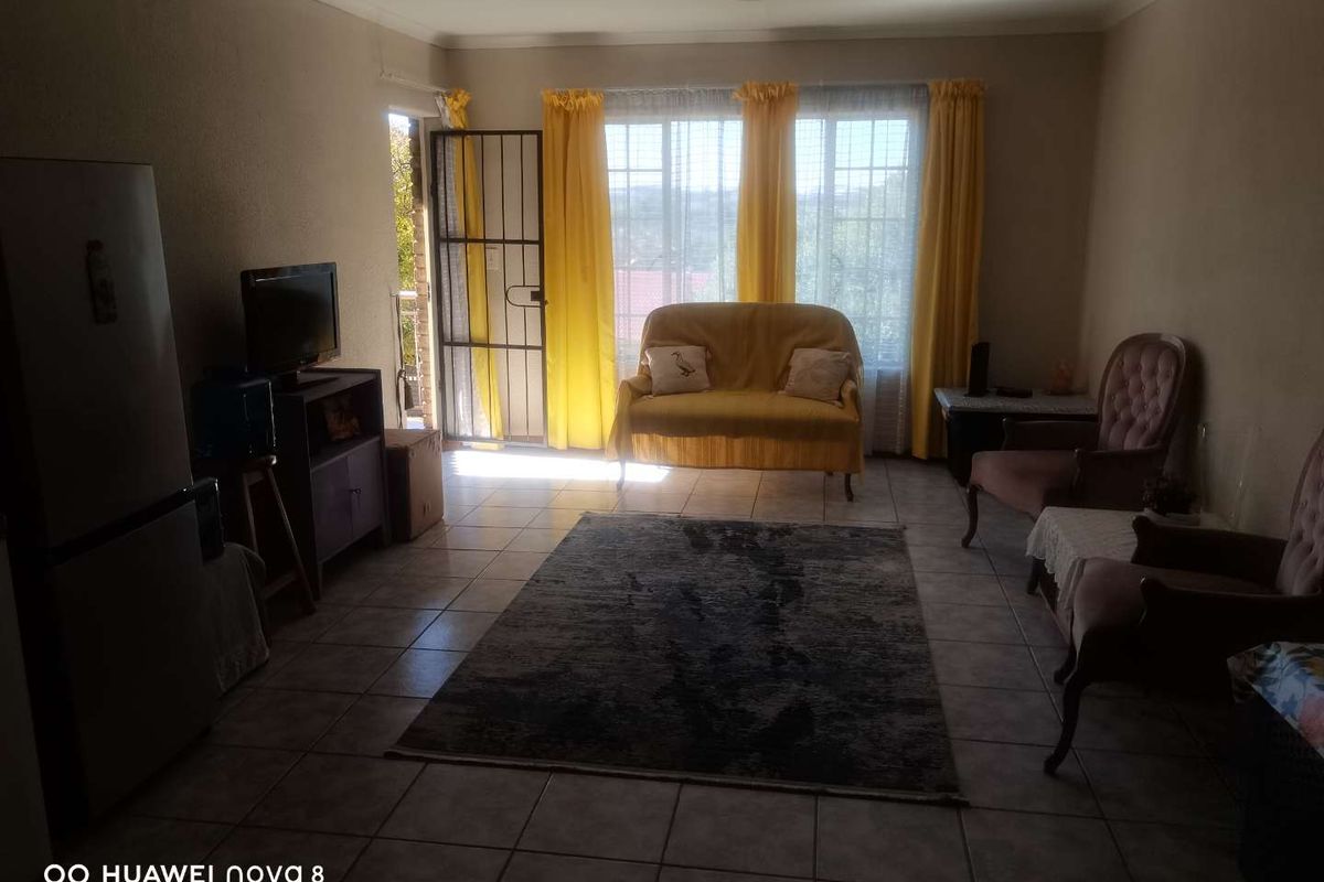 A living room featuring tiled flooring, large windows with natural light, and a security gate leading to an outdoor area.