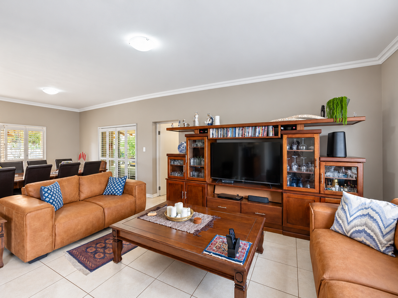 Spacious open-plan living area featuring neutral walls, tiled flooring, crown molding, and plantation shutters, providing a bright and functional space.