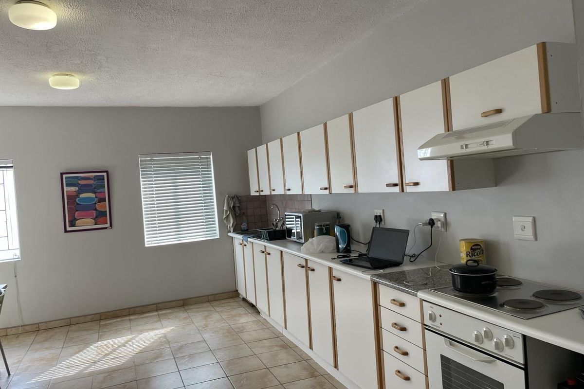 Functional kitchen featuring white cabinetry with wood trim, integrated oven, electric hob, extractor fan, and tiled flooring with ample natural light.