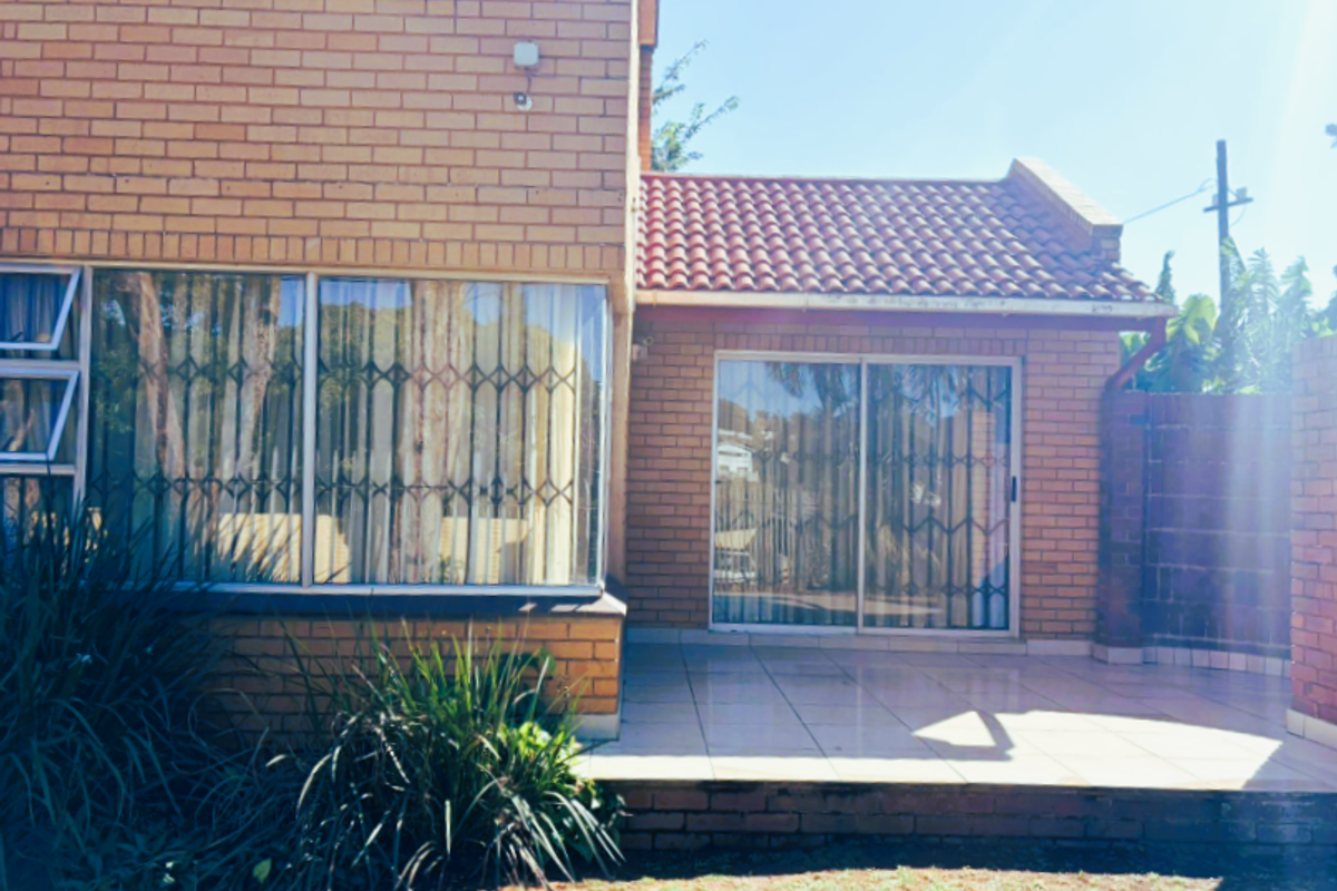 A rear view of the office building featuring a tiled patio area, brick facade, and sliding glass doors with security gates.