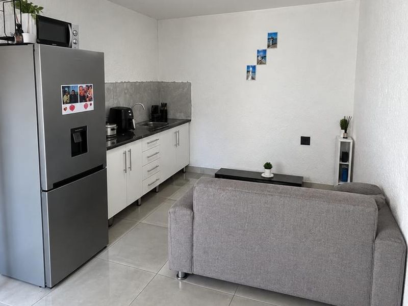 Compact open-plan living area featuring a modern kitchenette with white cabinetry, tiled flooring, and a functional layout suitable for efficient living.
