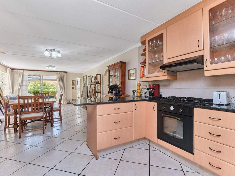 Spacious open-plan kitchen and dining area featuring light wood cabinetry, granite countertops, integrated appliances, and direct access to the outdoor patio.