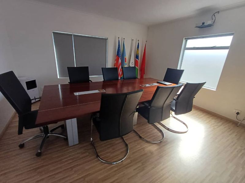A functional office boardroom featuring laminate flooring, roller blinds, and a ceiling-mounted projector, suitable for professional meetings and presentations.