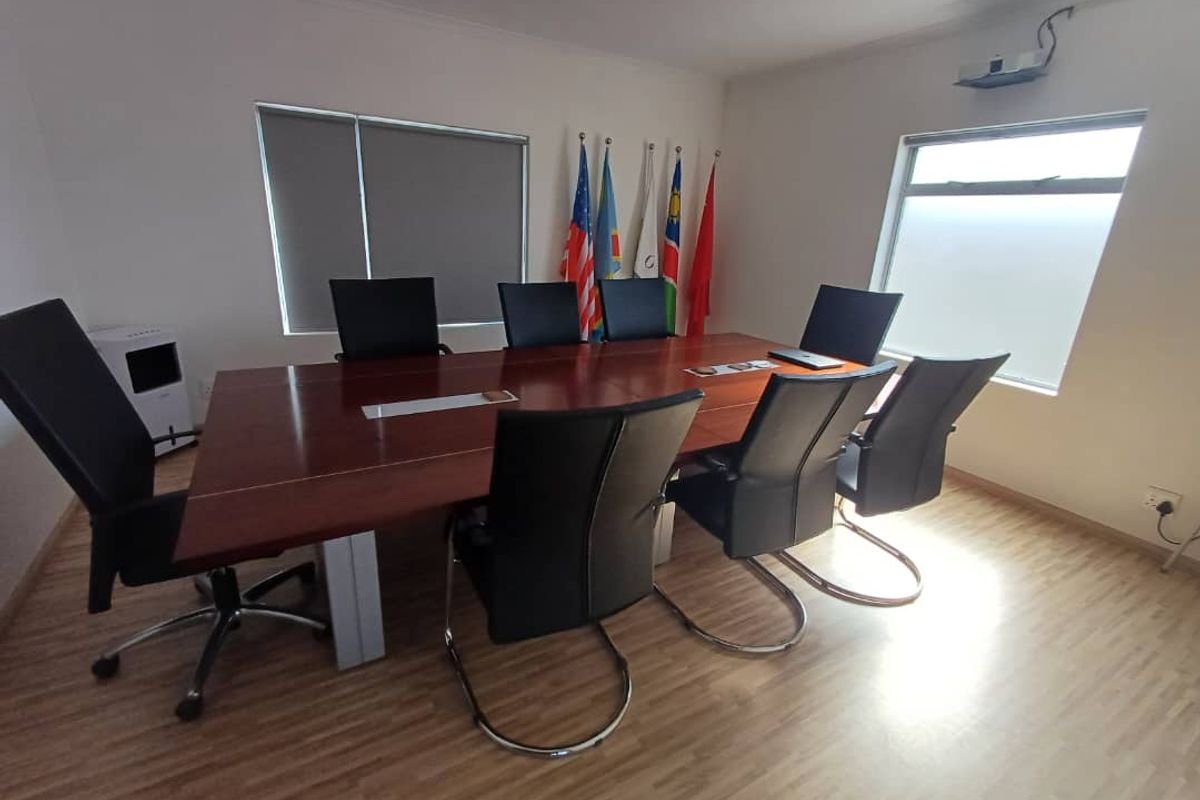 A functional office boardroom featuring laminate flooring, roller blinds, and a ceiling-mounted projector, suitable for professional meetings and presentations.