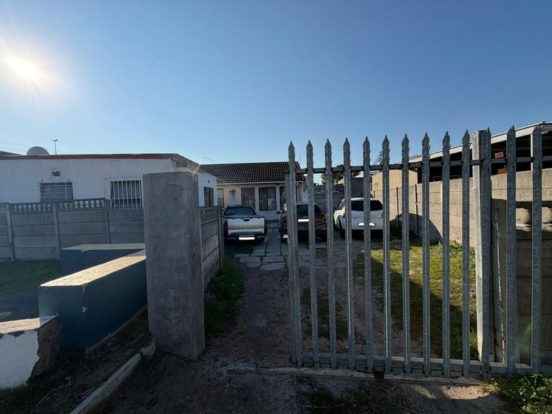 Front view of the property featuring a metal security gate, precast concrete boundary walls, and a paved driveway leading to the main entrance.