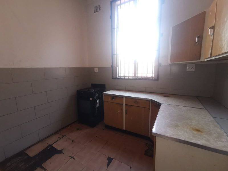 A dated kitchen featuring original cabinetry, laminate countertops, and a freestanding stove, requiring significant renovation and cosmetic updates to modernize the space.