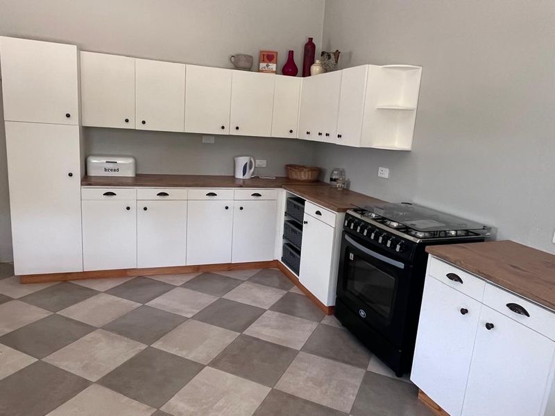 A functional kitchen featuring white cabinetry, wood-look countertops, a black freestanding oven, and a modern checkered tile floor.