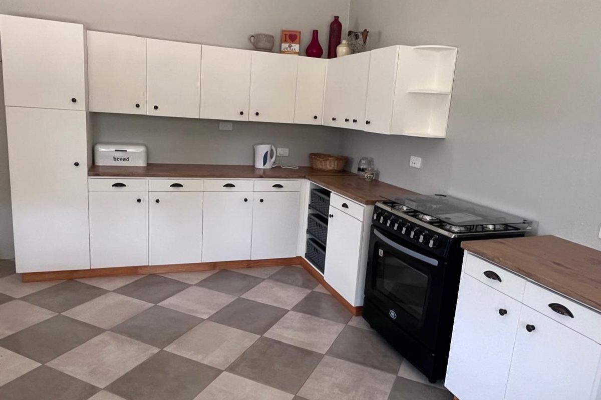 A functional kitchen featuring white cabinetry, wood-look countertops, a black freestanding oven, and a modern checkered tile floor.